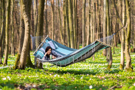 Happy healthy eating girl drinking green smoothie detox outdoors in hammock. Woman on weight loss diet vegan nutrition cleanse.の写真素材