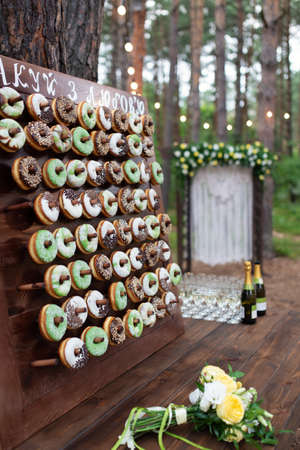 Delicious donuts on wooden stander. Wedding in the forest. Wedding decor. Donuts for guestsの写真素材