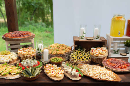 Tasty meals on a brown rustic wooden banquet table. Summer wedding in the forest