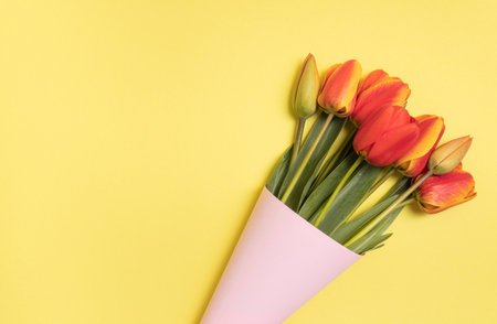 Bouquet of colorful tulips wrapped in a pink paper cornet on yellow background. Spring concept.の写真素材