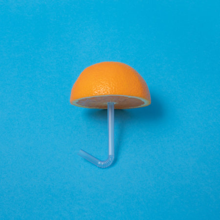 Orange stabbed on a drinking straw on blue background. Creative concept.の写真素材