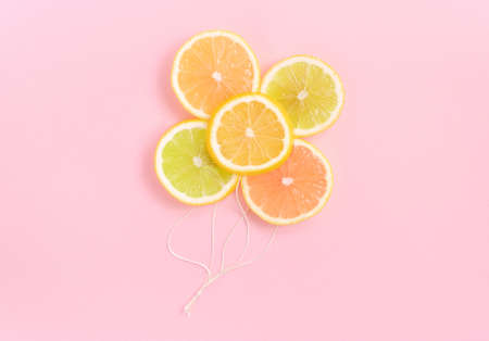 Lemon, orange, lime and grapefruit as balloons on pastel pink background. Fruity creative concept.