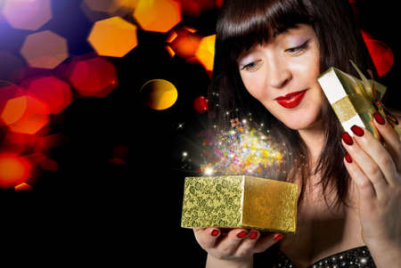 Beautiful Girl opens a gift in a small box golden festive night Holiday