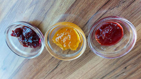 different types of jams in glass jars on wooden background, top view