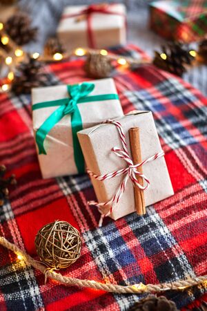 Christmas gifts on the background of a red woolen checkered plaid with garlands of cones and fir branches, a beautiful still lifeの写真素材