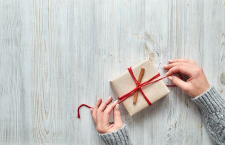 Female hands prepare gift wrap on a light wooden background