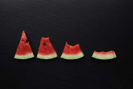 whole and eaten pieces of watermelon on a dark stone backgroundの写真素材