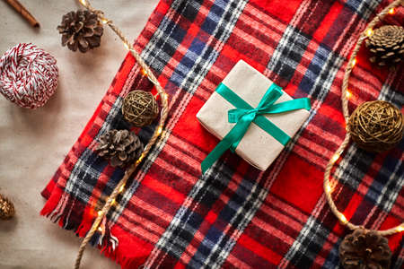 Christmas gifts on the background of a red woolen checkered plaid with garlands of cones and fir branches, a beautiful still lifeの写真素材