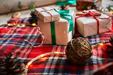 Christmas gifts on the background of a red woolen checkered plaid with garlands of cones and fir branches, a beautiful still lifeの写真素材