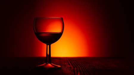 Silhouette of an empty glass wine or rum glass on a dark illuminated red backgroundの写真素材