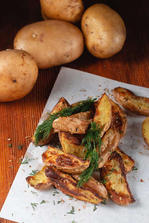 Delicious baked country potatoes with spices, dill and green onions, on a wooden tableの写真素材