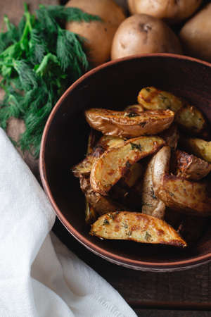 Delicious baked country potatoes in a earthen bowl with spices, dill and green onions, on a wooden tableの写真素材