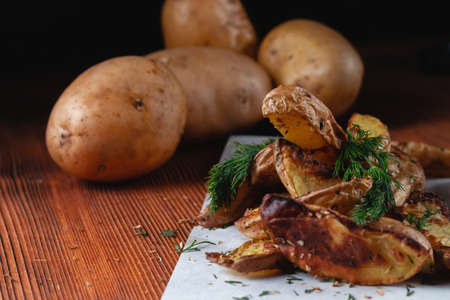 Delicious baked country potatoes with spices, dill and green onions, on a wooden tableの写真素材