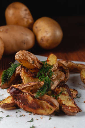 Delicious baked country potatoes with spices, dill and green onions, on a wooden tableの写真素材