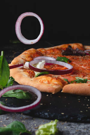 Traditional Italian pepperoni pizza with tomatoes, cheese and flying onions and herbs, on a table of dark slate on a black backgroundの写真素材