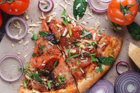 Slices Traditional Italian pepperoni pizza with tomatoes, grated metal cheese, onions and herbs, on a dark slate table with paperの写真素材