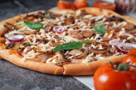 Homemade Italian pizza with mushrooms, ham, tomatoes, cheese, onions and herbs, on a dark slate stone table, space for text, selective focusの写真素材