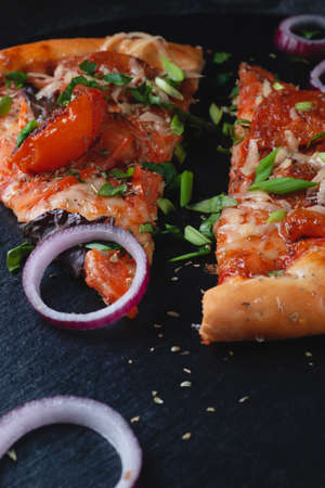 Slices Traditional Italian pepperoni pizza with tomatoes, cheese and flying onions and herbs, on a table of dark slate on a black backgroundの写真素材