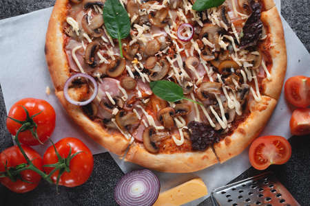 Homemade Italian pizza with mushrooms, ham, tomatoes, cheese, onions and herbs, on dark slate stone table, banner view topの写真素材