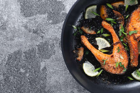 Juicy grilled salmon steak with lemon, spices and lime in a pan on a natural slate stone table, close-up. Deliciously cooked salmon filletの写真素材