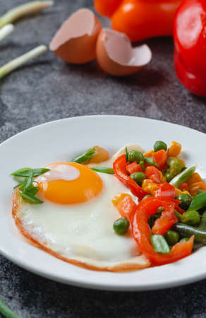 Fried eggs and vegetables in a white plate on a gray concrete stone table for breakfastの写真素材