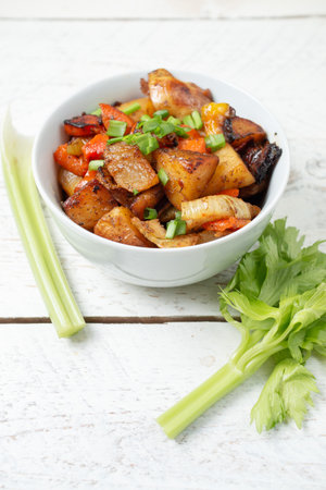 Diced cooked vegetables on light wood background in white plate. Healthy lunch - stewed garden vegetables. Traditional ratatouille with greens, zucchini, bell peppers and eggplant. Space for textの写真素材