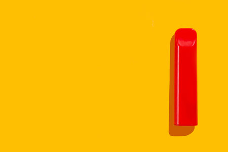 Disposable red e-cigarette on yellow isolated background. The concept of modern smoking, vaping and...