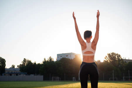 Sport and wellness. Fitness girl in white sneakers doing stretching workout. Fashion sporty woman with strong muscular body training. Fit female stretching at outdoor stadiumの写真素材