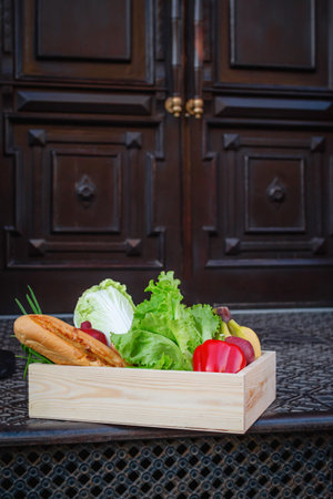Contactless food delivery. Apartment entrance with delivered box. Control Epidemic Prevention measures of virus. Self isolation banner. Wooden food box left in front of the houseの写真素材