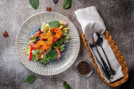 Serving a dish from the restaurant menu. Royal shrimp in batter with lemon and salad on a plate against a gray stone table, a tasty appetizerの写真素材