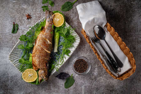 Roasted Whole Trout with lemon, lettuce and dill and parsley greens on a plate against a gray stone tableの写真素材