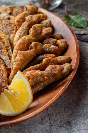 An appetizer in a restaurant, fried sprat on a wooden plate with lemon and cream sauce against a...