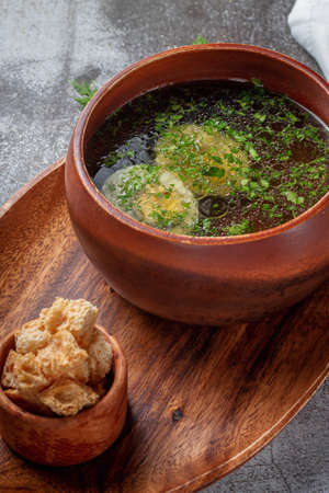 Chicken soup with boiled egg sprinkled with dill and parsley greens in a wooden bowl with bread...