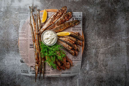 An appetizer in a restaurant, fried sprat on a wooden plate with lemon and cream sauce against a gray stone tableの写真素材