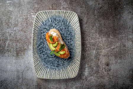 Fried shrimp and avocado sandwich on a plate of greens against a gray stone tableの写真素材