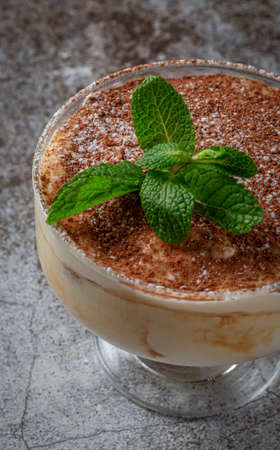 Classic tiramisu dessert with mint leaves in a glass, with cocoa and chocolate in the background of a gray stone tableの写真素材