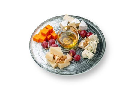 An appetizer on the restaurant menu. An assortment of cheese with nuts, honey and grapes in a plate on a white insulated backgroundの写真素材