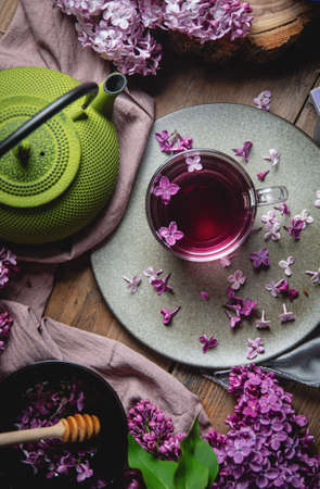 The concept of homeliness. Living room interior in the style of hygge, a cozy still life, a cup of hot tea with lilacs on a dark background and a cast-iron kettle, light from the windowの写真素材