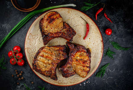 Grilled pork loin, pork steak on the bone on a dark stone table with vegetables, cream and tomato sauce. Served on a clay plate. Fast food restaurant, delivery service.の写真素材