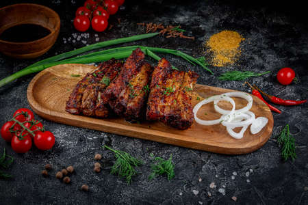 Grilled pork ribs on a dark stone table with vegetables, cream and tomato sauce. Served on a wooden board. Fast food restaurant, delivery services.の写真素材