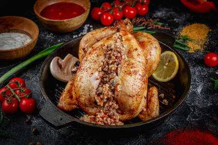 Grilled chicken stuffed with buckwheat on a dark stone table with vegetables, cream and tomato sauce. Served in a frying pan. Fast food restaurant, delivery service.の写真素材