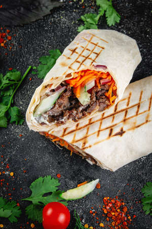 Shawarma, burrito cut with vegetables and herbs on a dark stone table. The concept of fast food...