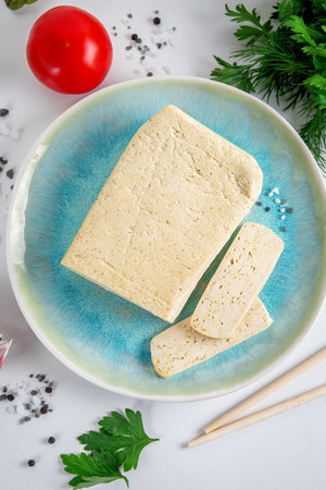 Sliced tofu soy cheese on a cutting board with basil, spices and vegetables
