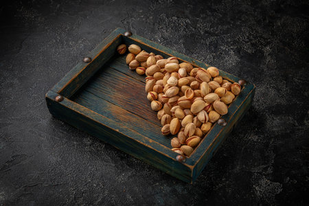 Beer snacks, pistachio nuts in a wooden box on a dark tableの写真素材