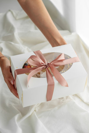 Young girl pastry chef holding a gift box with ribbons on a light backgroundの写真素材