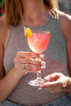 Young woman holding an alcoholic cocktail with vodka, cranberry morsels, triple sec, lemon juice, sugar syrup, sunny hard lightの写真素材