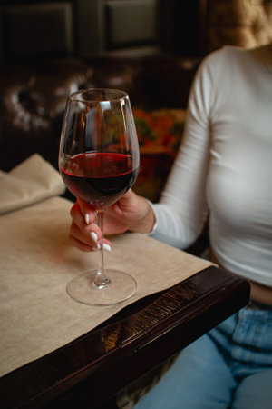 Hand holding a glass of red wine in a cozy bar settingの写真素材
