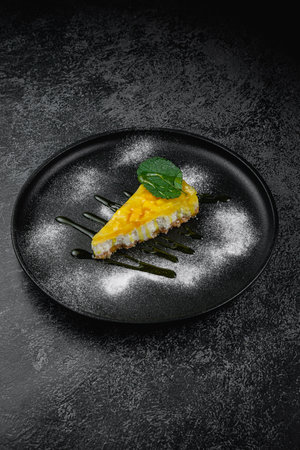 Lemon cheesecake with mint leaf in a dark plateの写真素材