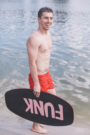 boy standing with skim board and smilingの写真素材