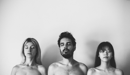 three naked people standing with closed eyes behind the wallの写真素材